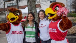Rocky and Roxy the red hawks pose with two smiling students