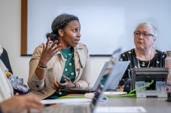 A woman in a group setting speaks to her peers around a conference table