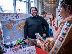 Student stands next to poster display as another student approaches their table smiling at International Mother Language Day