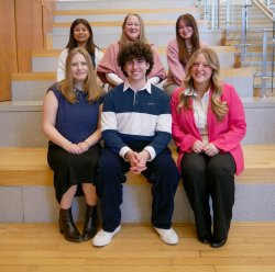 Six people dressed professionally in two rows of three sitting on stairs. They are smiling.