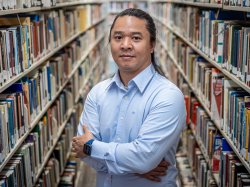 Kaung Hla Zan stands between two long shelves of books in a library.