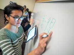Student with glasses practicing writing Chinese on a white board in class.