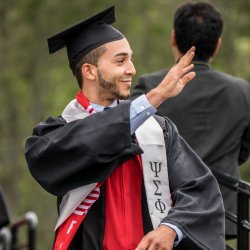 Image of a Justice Studies student waving to the crowd and wearing a cap and gown at a convocation ceremony.