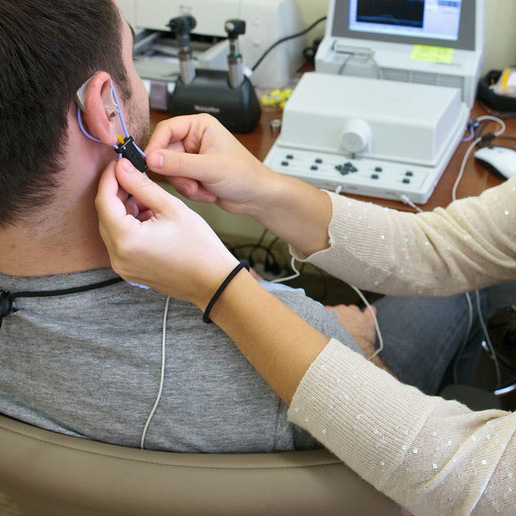 Audiology student placing hearing device on man's ear with audiology equipment in the background