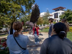 Female student ambassador conducting a tour and standing in front of the Red Hawk Statue on campus