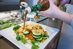 A closeup of hands pouring salad dressing on a salad.