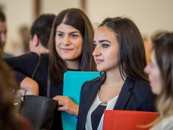 Woman talking to another person while holding a folder at a conference.