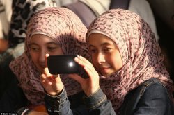 women in head scarves taking photo with phone