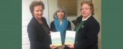 Three women standing at a book event holding two copies of a book.