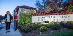 Students walking past Montclair State University entrance sign at dusk.