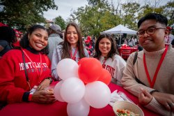 four alumni standing at a table with a red and white balloon centerpiece