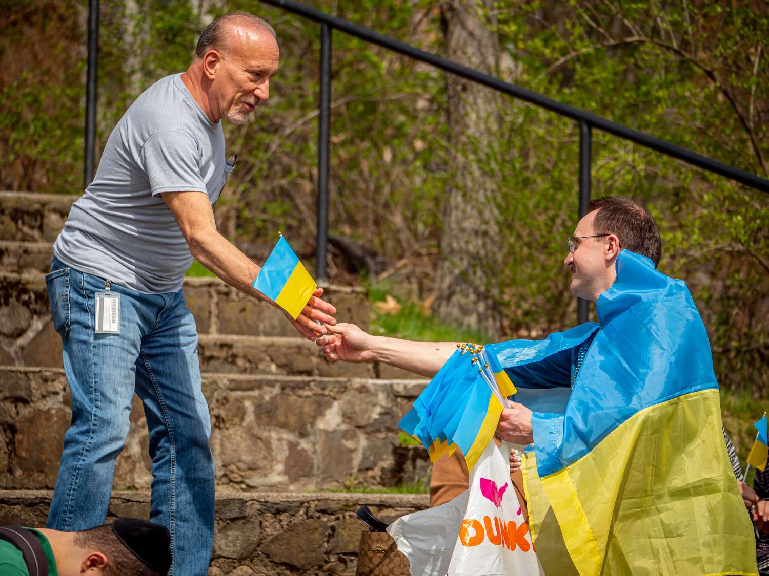 Man draped in ukranian flag hands small flag to another man.