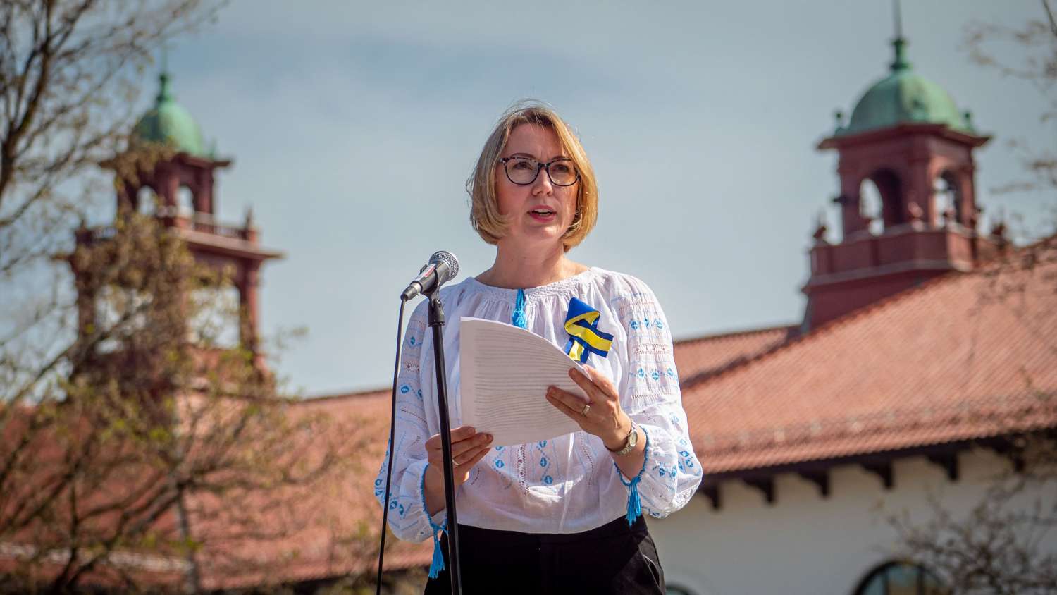 Woman at microphone delivering a speech with cole hall belltowers in the background
