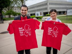 A man and a woman hold up their Red Hawk Day t-shirts.