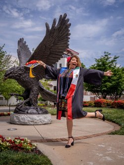A graduate celebrates in front of the Red Hawk statue.