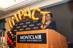 Imani N. Hayes at a lectern in front of the word IMPACT spelled with balloons.