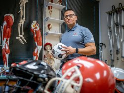 Luis Torres holds a soccer ball in a classroom filled with sports equipment.