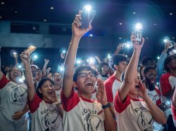 A group of students shine flashlights on their cell phones.