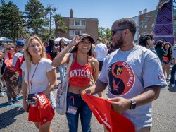 Two Montclair State University students and one Bloomfield College student stand together, chatting at an outdoor carnival.