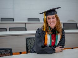 Jean-Marie Beeks sits in a classroom in her graduation cap and gown.