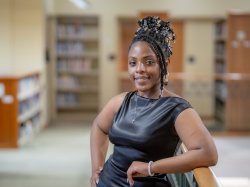 Lataiva Balmer, a Psychology major and member of the first graduating class of Bloomfield College of Montclair State University, is shown in the library, wearing a black dress.