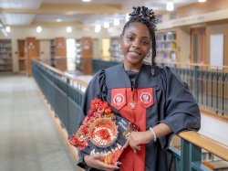 Lataiva Balmer, a psychology major and member of the first graduating class of Bloomfield College of Montclair State University, is shown in the college library wearing her cap and gown on the Bloomfield campus. She holds a decorated graduation cap.