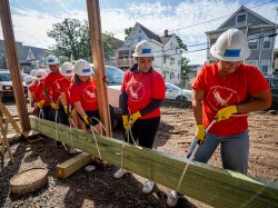 students wearing construction helmets, carrying a wood beam with rope hoists