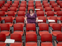 A student sits in the center of a lecture hall filled with red chairs.