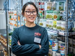 Kaori Sakae stands, arms crossed, in front of food-filled shelves at Red Hawk Pantry.