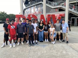 Students standing and smiling in two rows outside of a soccer stadium.