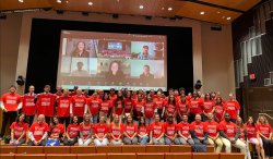 A group of people in three rows on a stage in red t-shirts.