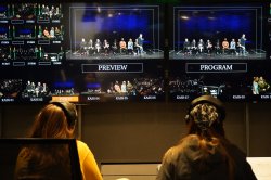 Two people working on a TV production project, wearing headphones and looking at monitors, with their back to the shot.