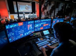 A student in front of several TV production monitors, controlling audio and visual elements of a show.