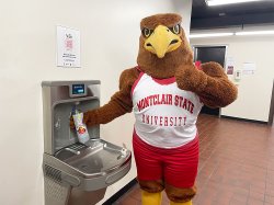 Rocky the Red Hawk filling a water bottle at a bottle filler with a Fill it Forward sign.
