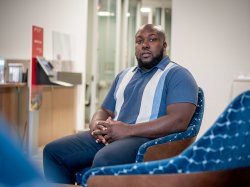 Black male student sitting in chair for posed professional headshot.