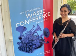 Karina Bloom holding a fluet next to a banner reading Wasbe Conference