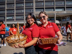Two students in red T-shirts holding baskets in front of Montclair State's Blanton Hall building