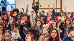 A large group of female students raise their hands in the air.