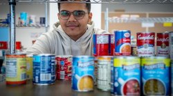 A male student peers through a shelf of canned food