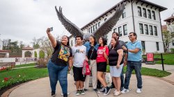 Seven people pose for a selfie in front of the hawk statue on campus.