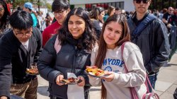 Two students smile as they hold plates of food at an outdoor event.