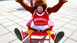 A student in a Red Hawk costume sits in a chair, exposing their face.