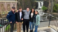 A professor and four students stand in front of a waterfall.