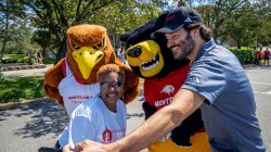 Two college mascots - a bird and a bear - pose for a selfie with a man and a woman.