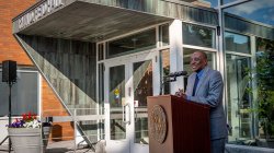 former President Irvin D. Reid stands at a podium in front of the Irvin D. Reid Hall entrance.