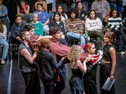 Five actors carry an actor wrapped in cloth as the audience during a performance of Richard III.