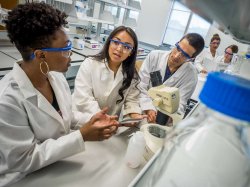 Photo of teacher and students wearing lab coats by a microscope.