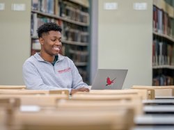 Student in library using laptop with redhawk sticker on it