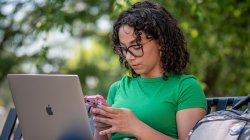 Student checking their phone and with their laptop open.