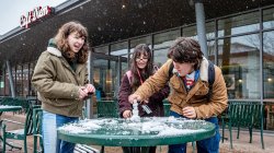 three students making a mini snowman on a green metal table outside of Cafe Diem on the Montclair campus